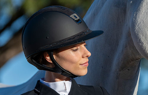 Frau mit Samshield Miss Shield Reithelm und weißem Pferd im Hintergrund